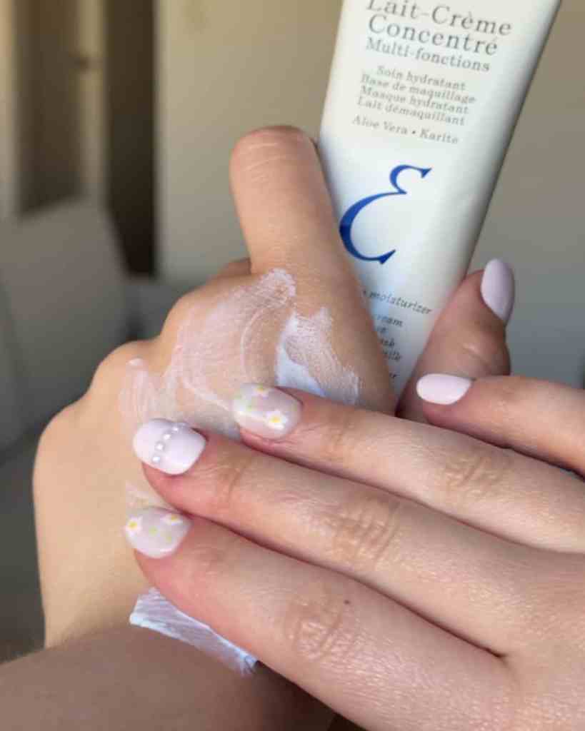 Close-up of hands applying White Rabbit Social hand cream with floral nails and textured cream on skin.