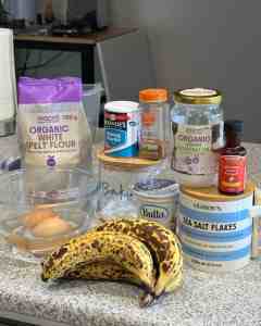 ALT text: Fresh bananas, flour, baking powder, coconut oil, vanilla extract, eggs, and sea salt flakes.