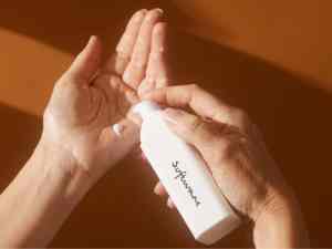 Close-up of hands applying skincare lotion with a white pump bottle labeled "suitcase".