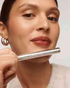 Close-up of a woman with bold lipstick holding a silver lipstick tube.