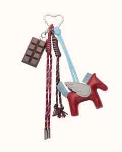 trending bag charm with chocolate and red hoarse as a luxury gift idea for women who have everything on a light pink background 