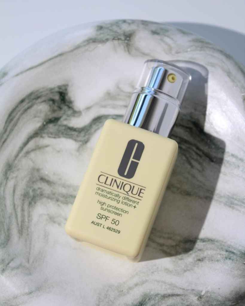 A close-up of Clinique SPF 50 moisturising lotion with high protection, placed on a marble surface for skincare routine enhancement.