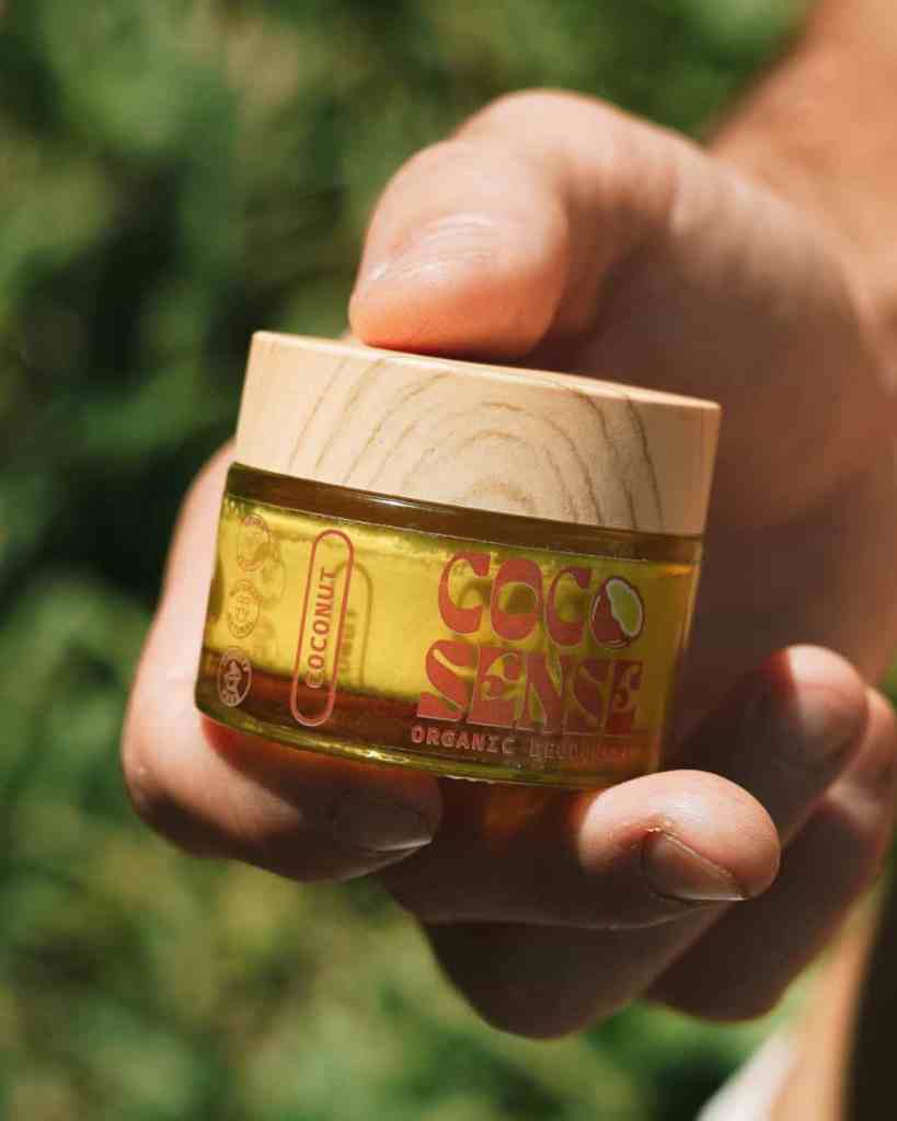 Close-up of a hand holding a coconut-scented organic lip balm with a wooden lid, highlighting natural ingredients and eco-conscious packaging.
