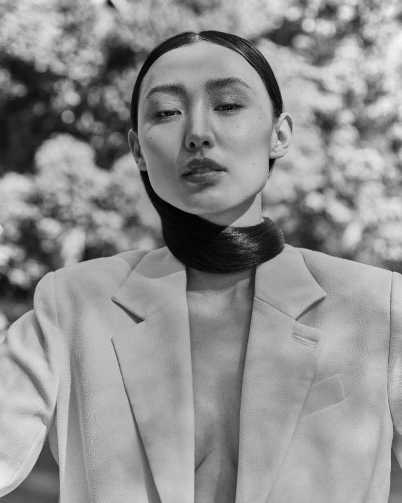Stylish woman with smooth hair, wearing a blazer, posing outdoors in natural light.