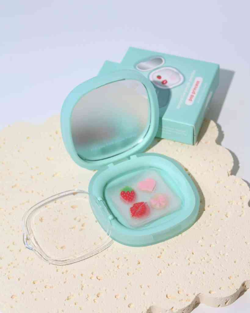 Image shows a pastel blue compact mirror with a heart, strawberry, and flower soap, on a textured surface.