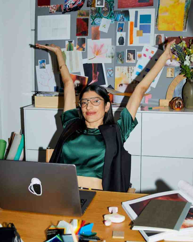Woman smiling at desk with vibrant mood board background.