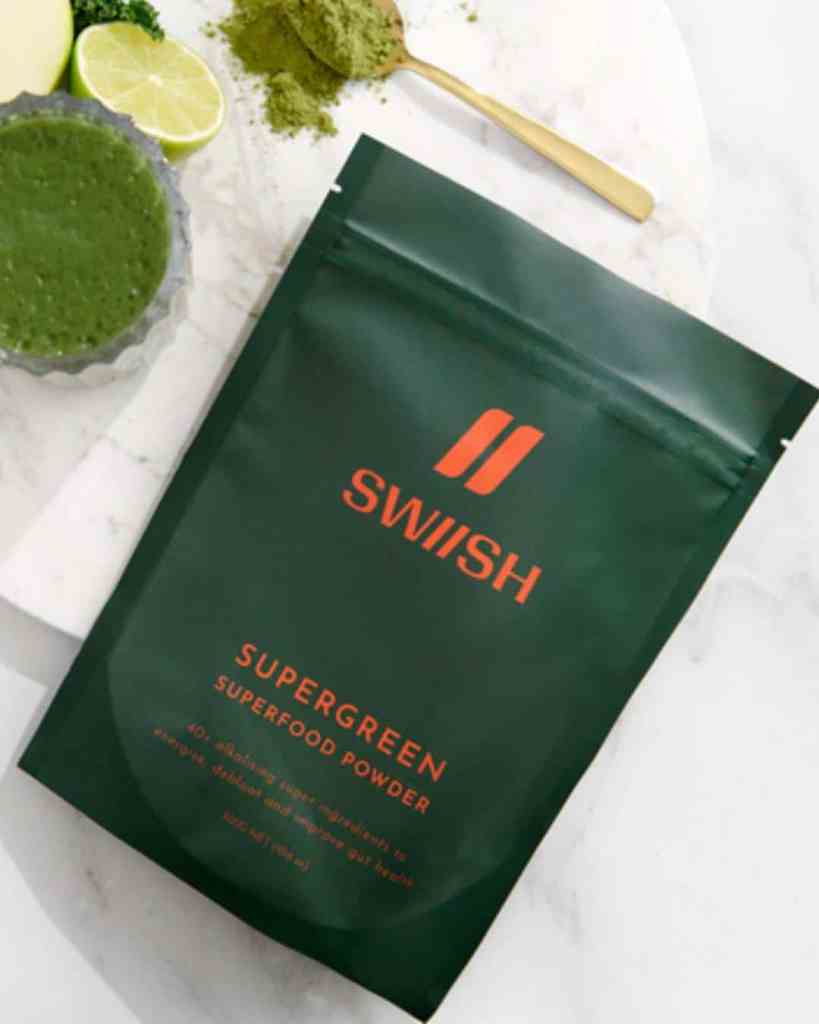 Bright green superfood powder in packaging on white marble surface with lime and matcha spoon.