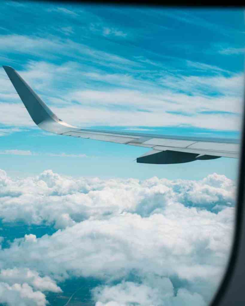 Airplane wing flying above clouds, representing travel and aviation services by White Rabbit Social.