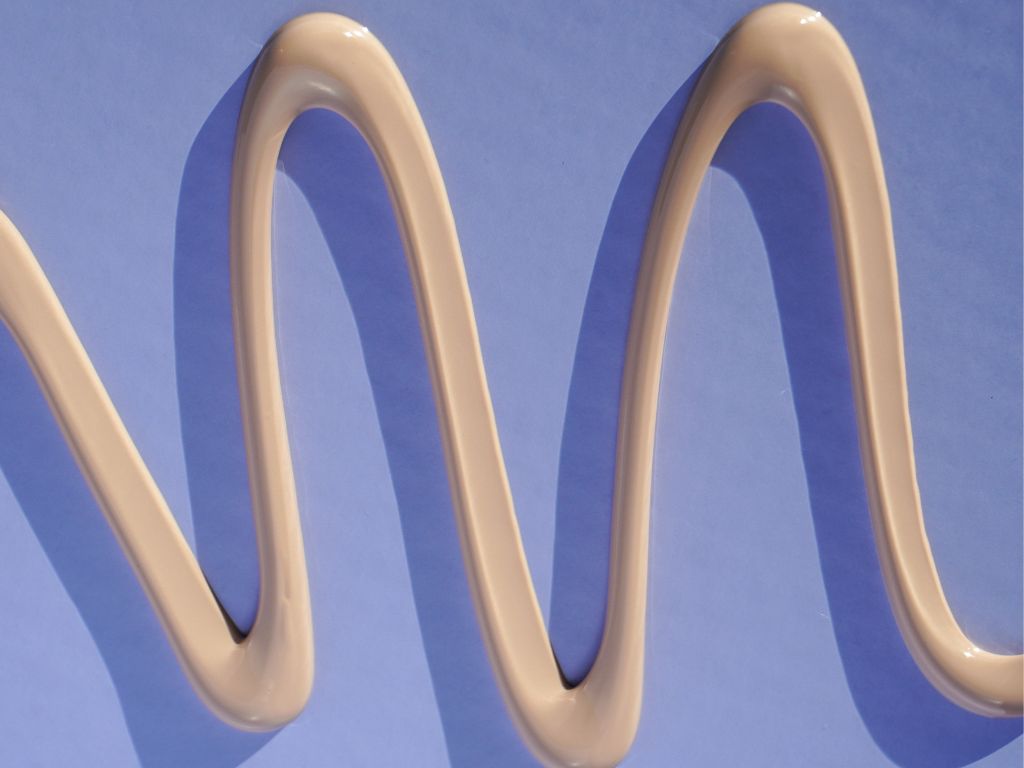 Close-up of the Naked Sundays BeautyBarrier SPF50 texture, a creamy, lightweight zinc sunscreen formula shown in a swirl on a blue background