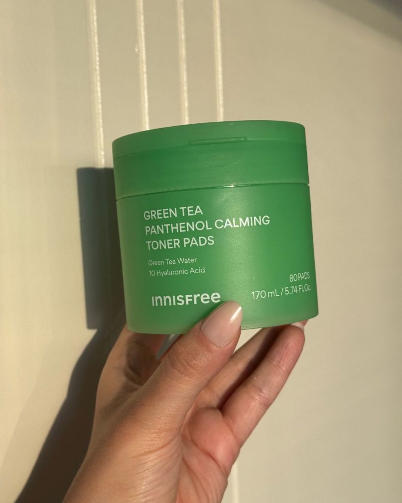 innisfree Green Tea Panthenol Calming Toner Pads tub held against a white panelled wall